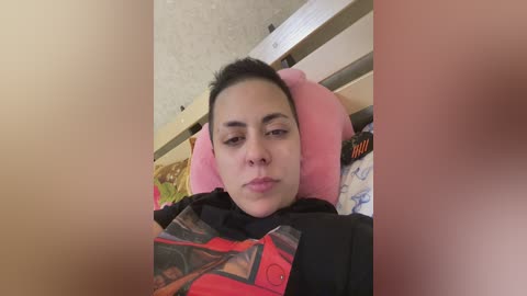 Video of a young woman with medium skin tone and straight black hair, lying on a pink pillow in a bed with patterned sheets.