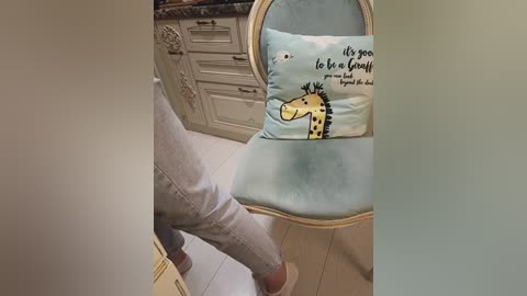 A video showing a person in light gray pants standing in a kitchen with a giraffe cushion on a chair. The background features white cabinets and a granite countertop.