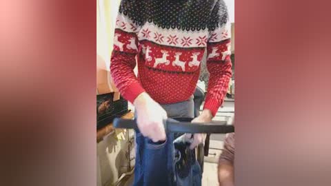 Video of a person in a red and black Nordic sweater, holding a black shopping cart, in a grocery store aisle with shelves and products visible in the background.