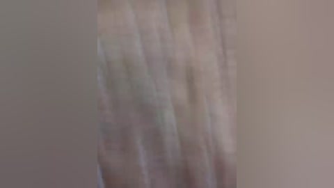A blurry video of a person standing in front of a beige wall. The subject's body and facial features are indistinguishable due to the extreme blurriness, making it impossible to discern any specific details.