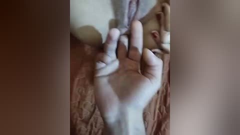 A video showing a close-up of a nude female's hand holding her exposed vulva, set against a textured, brown fabric background. The image is blurred, focusing on the hand and genitalia, with no identifiable facial features.