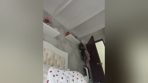 Video of a modern bedroom with a white tufted headboard, white shelves, and a dark wooden door. The room has a minimalist decor with a white wall and pink flowers.