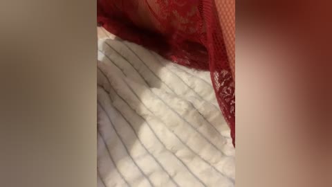 A video featuring a close-up of a white, quilted blanket with a subtle marbling pattern and a red lace fabric draped over it. The scene is dimly lit, creating a soft, cozy atmosphere.