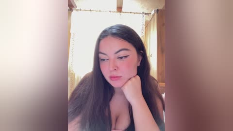 Video of a Latina woman with long, straight brown hair and a fair complexion, wearing a black top, resting her chin on her hand in a thoughtful pose.
