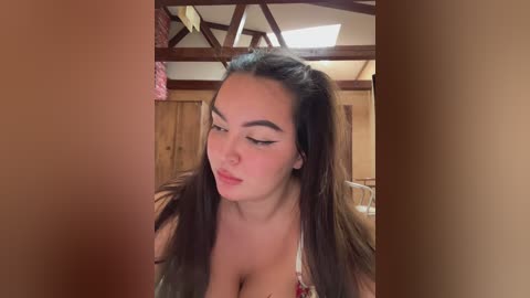 Video of an Asian woman with long dark hair styled in pigtails, wearing a low-cut white top, looking down with a thoughtful expression.