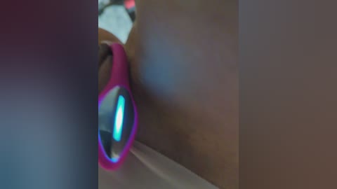 A close-up video of a bright pink, glowing, oval-shaped electronic device with a small blue light, resting on a textured, brown wall. The background is blurred, creating a soft focus effect.