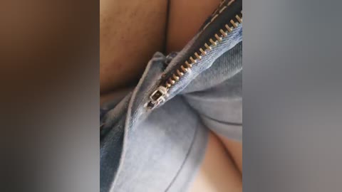 A close-up video of a person's lower torso, showing the seam of light blue denim jeans with a metal zipper partially open. The background is blurred, highlighting the texture and fabric of the jeans.