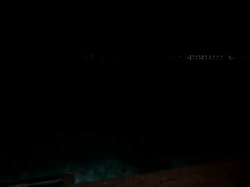 A dimly lit, dark video of a pool at night, with barely visible, scattered lights in the background. The foreground is a shadowy, indistinct area, creating a mysterious, eerie atmosphere.