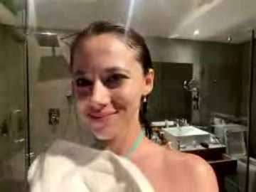 Video of a smiling, wet-haired woman with a towel wrapped around her shoulder, standing in a modern bathroom with sleek, silver fixtures.