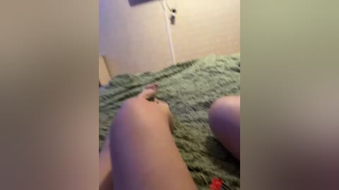 A video of a person lying on a green, textured rug in a beige room. The person's bare legs are visible, with a red sock on one foot.