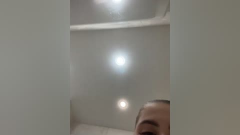 Video of a man with light skin, short dark hair, and brown eyes, partially visible in a small, dimly lit, narrow space with white walls and ceiling.