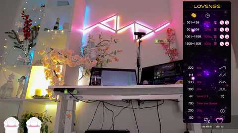 A video of a cozy, pastel-themed room with a white desk, pink floral decorations, and neon triangle lights. A digital overlay shows \"Love Sense\" and stats.