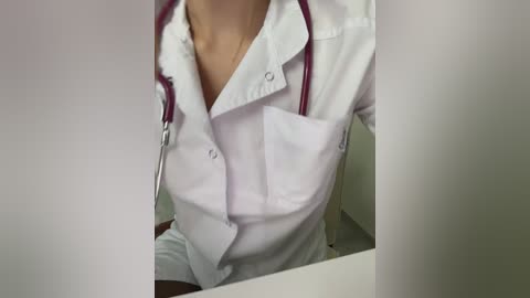 Video of a woman in a white lab coat with red stethoscope, sitting at a desk, wearing a white top and black pants.