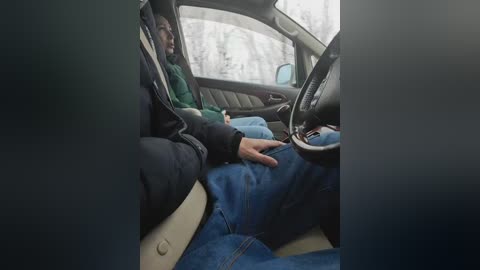 A video showing a person wearing a green jacket and jeans, sitting in the driver's seat of a car, with a snowy forest background through the window.