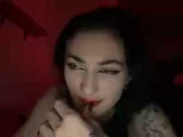 A video of a woman with long black hair, pale skin, and red lipstick, seductively licking her fingers in a dimly lit red room.