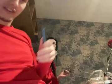 A video captures a person with a red shirt holding a parakeet, with a patterned wall and cluttered background.