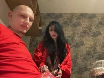 Video of a bald man in a red shirt and a woman with long black hair and a red robe, standing in a rustic room with stone walls.