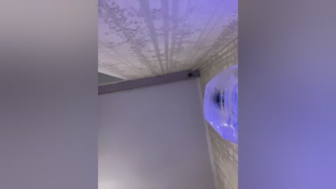 Video of a modern, dimly lit bathroom with a cylindrical, translucent blue bathtub in the foreground, surrounded by textured, light-colored walls.