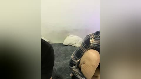 Video of a dimly lit, cluttered bedroom with a beige carpet, a white pillow, a plaid shirt, and a black object partially obscuring the view.