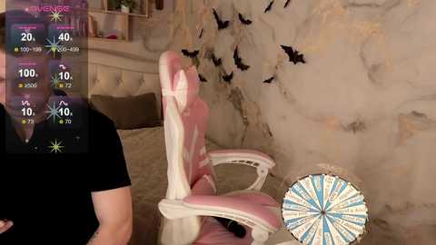 Video of a pink gaming chair with a white cushion, placed in a dimly lit room with a textured beige wall and a dartboard.