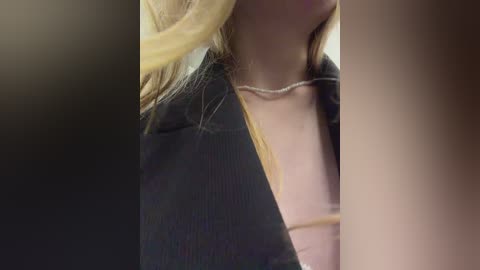 Video of a close-up of a woman's neck and shoulders, showing long blonde hair, a black jacket, and a silver necklace. The background is blurred, focusing attention on the subject.