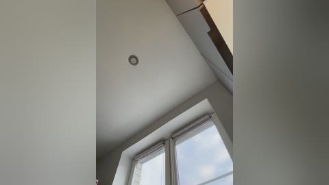 Video of a modern, minimalist interior space featuring a ceiling light and large windows with sheer curtains. The walls are painted in a soft, neutral color, contributing to a clean, airy atmosphere.