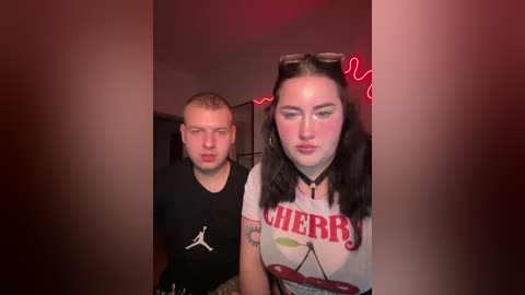 Video of a young woman with long black hair, wearing a white \"Cherry\" T-shirt, and a man in a black shirt, standing in a dimly lit room with neon lights and a \"Juicy\" sign.