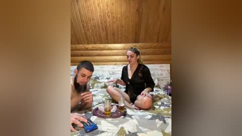 A video depicts a bearded man in a black robe, sitting on a patterned rug, pouring honey over a baby's head. The background features wooden walls and a wooden ceiling.