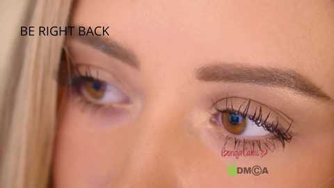 Video of a close-up of a light-skinned woman's eye, with a brown eyebrow, long eyelashes, and a faint shadow highlighting the upper lid. Text overlays read \"BE RIGHT BACK\" and \"Genioplasty.\