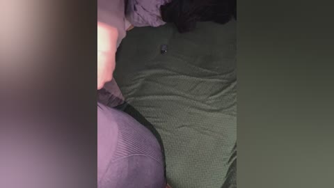 Video of a person lying on a bed, wearing a dark green, textured top and black leggings. The room is dimly lit, creating a soft, intimate atmosphere.