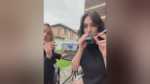 Video of two women in black outfits, one with a camera and another with a microphone, standing in front of a brick building with a sign, recording in a suburban neighborhood.