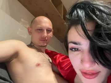Video of a bald, muscular man with a beard and a red shirt, and a woman with dark hair and red lipstick, both posing intimately.