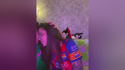Video of a woman with long brown hair, wearing a Barcelona football jersey, in a dimly lit room with wallpaper and plush toys.