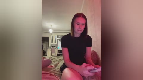 Video of a young woman with straight, light brown hair, wearing a black t-shirt, playing a video game on a couch in a dimly lit room.