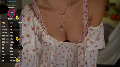 A close-up video of a light-skinned woman in a low-cut floral dress, with a necklace, showcasing cleavage. Background shows an app interface with stats and icons.