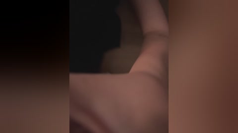 A blurry video of a person lying on their back, arms raised, against a dark background, with visible light skin tones and indistinguishable clothing details.
