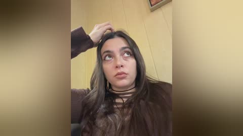 Video of a young woman with long brown hair, wearing a dark brown sweater, sitting indoors. A person's hand is gently touching her head, creating a comforting moment.