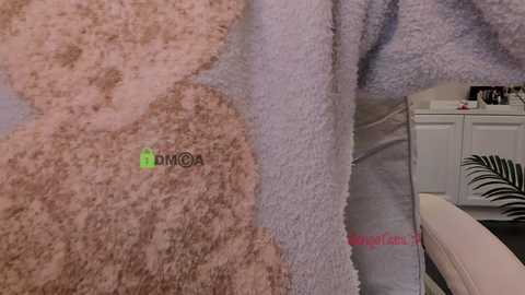 Video of a fluffy, light pink bathrobe with a subtle green logo and a white zebra-print pillow on a bed.