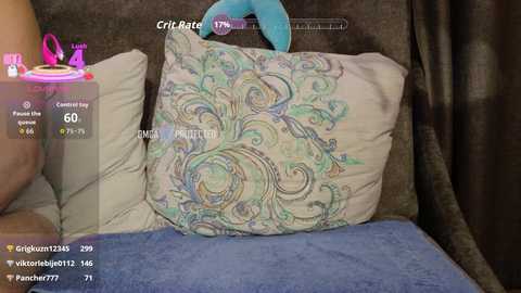 Video of a woman's hand holding a blue and green plush toy on a gray bedspread. She's wearing a white shirt, and there's a digital display showing her \"crit rate\" at 70%.