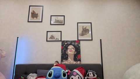 Video of a cozy bedroom with a grey sofa adorned with plush toys, a wall featuring framed artwork and a large, colorful painting of a woman with a crown.