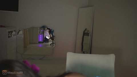 Video of a dimly lit, minimalist bedroom with a mirror, white chair, and a purple-pink hair tie visible in the foreground.