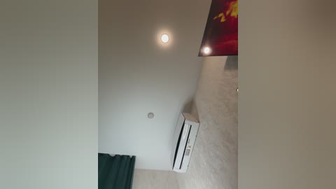 Video of a modern, minimalist room with a white ceiling and a small, round ceiling light. An air conditioner unit is mounted on the wall, partially covered by a green curtain.