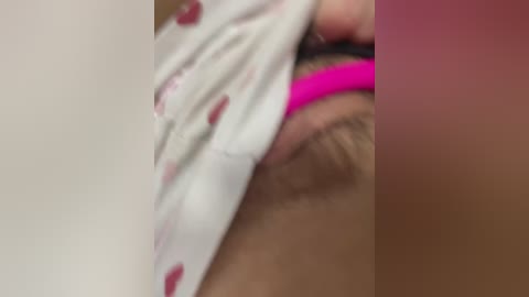 Video of a close-up of a person's hand holding up a white fabric with pink heart prints, revealing a partially shaved pubic area with visible hair. The background is a gradient of pink to red.