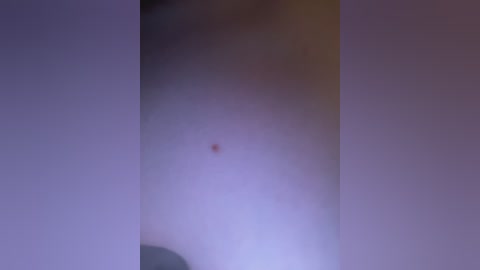 A blurred video of a person's chest with a small mole in the center, surrounded by soft, purple lighting.