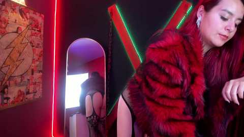 A video of a young woman in a red fur coat, standing in a dimly lit room with a large mirror reflecting her bare backside.