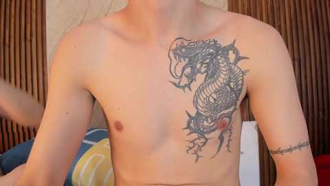 Video of a shirtless, light-skinned young man with a detailed black dragon tattoo on his right shoulder, standing in front of bamboo walls.