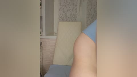 Video of a close-up of a person\u2019s arm and shoulder in a room with beige walls and a light blue shirt.