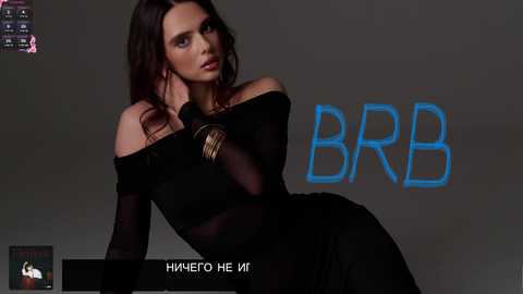 Video of a slim, brunette woman with long hair, wearing a sheer black off-shoulder dress and gold bracelets, posing against a dark gray backdrop with \"BBB\" text and \"HUMAERO HE MIT\" caption.