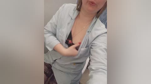 Video of a light-skinned woman with a medium build, wearing a light blue blazer, revealing a black bra with red lace detailing, and dark patterned pants.