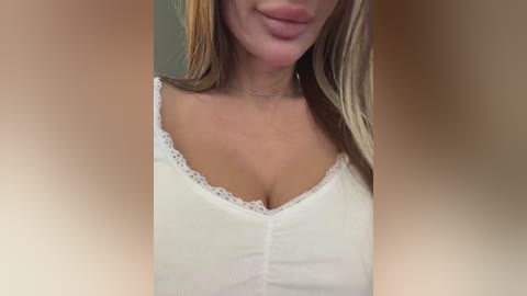 Video of a light-skinned woman with blonde hair, wearing a white lace-trimmed top, smiling, with blurred background.